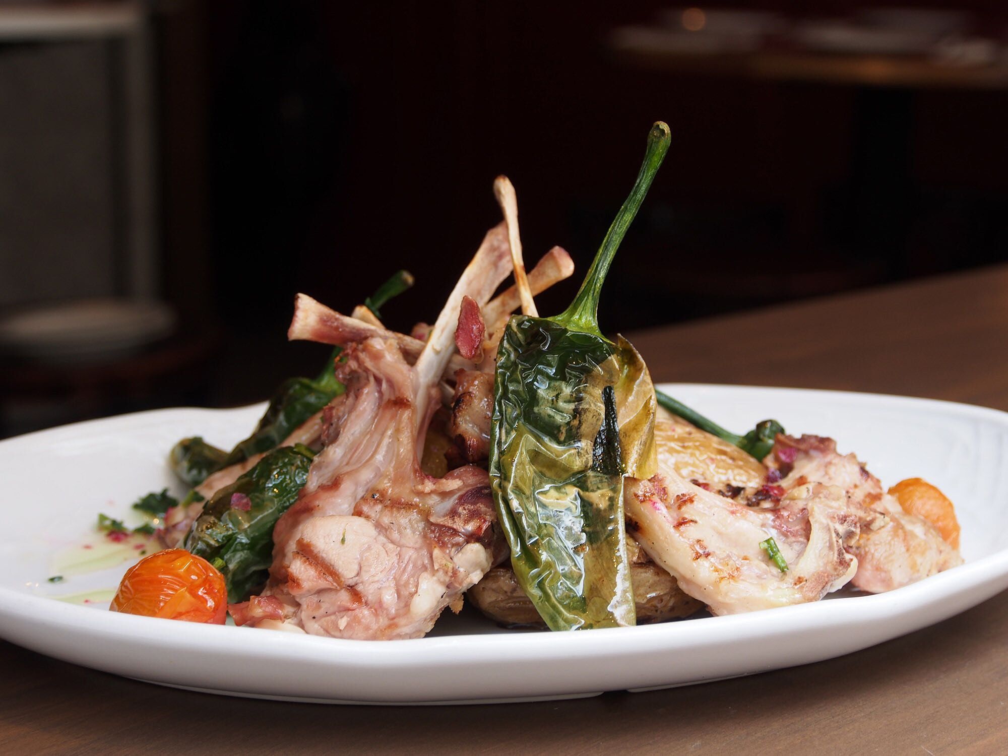 Plato de carne a la parrilla con pimientos verdes y tomates cherry sobre mesa de madera
